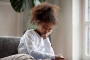 A child sitting on a couch with her chin in her hand, looking sad